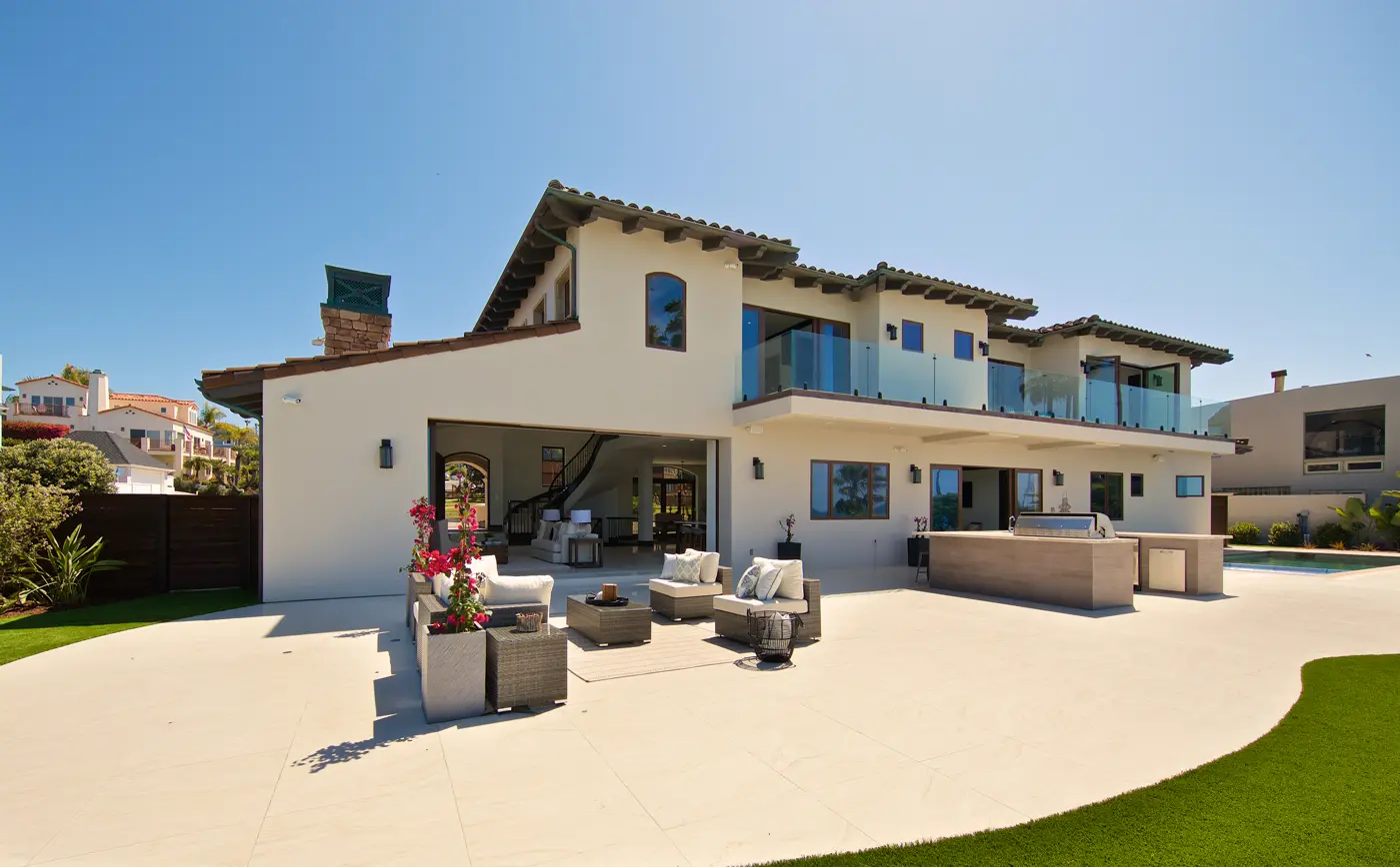 Coastal custom home exterior with folding glass walls opening onto a poured-concrete patio and lawn