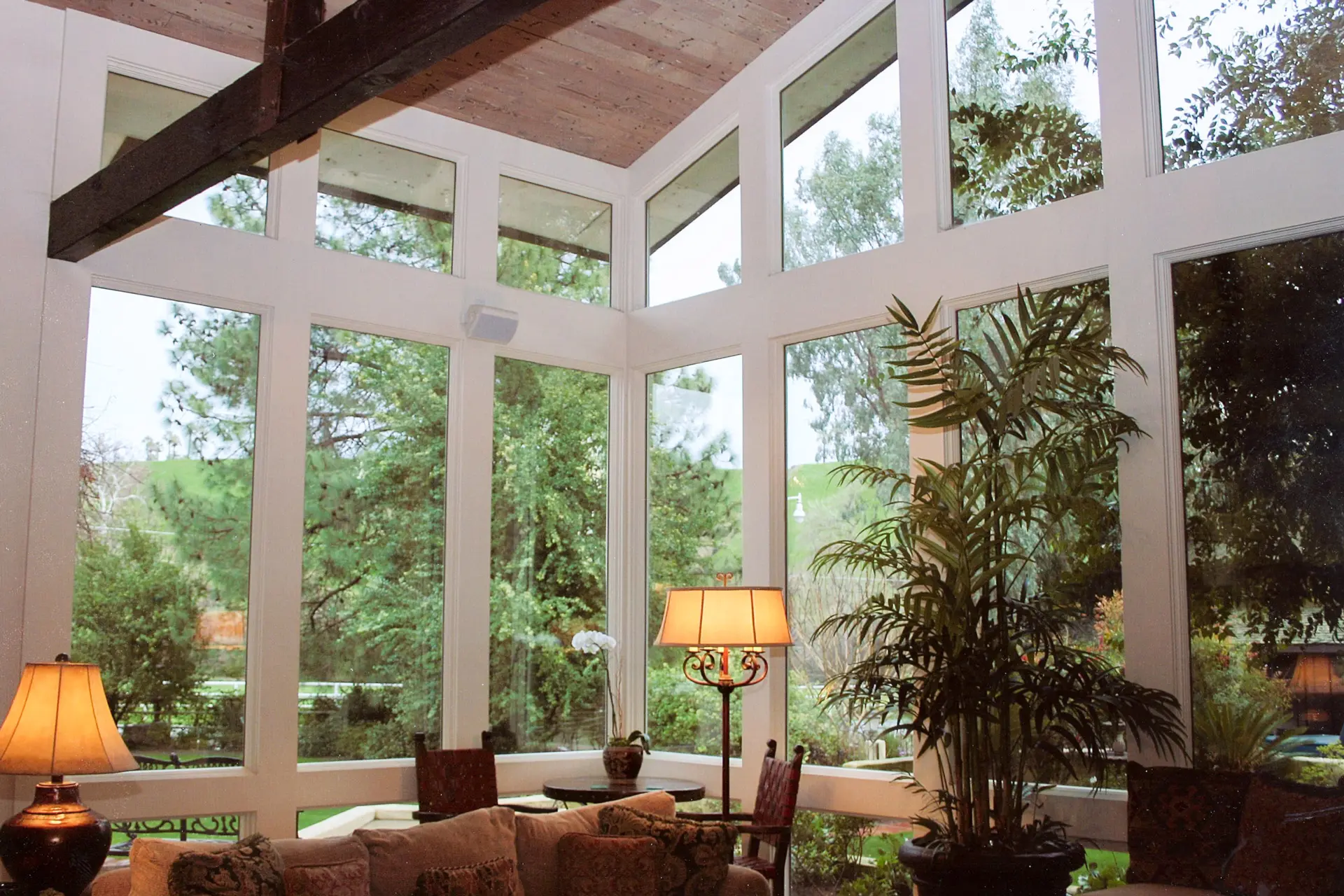 Great room with a two-story window wall, exposed timber beam, and garden views on three sides