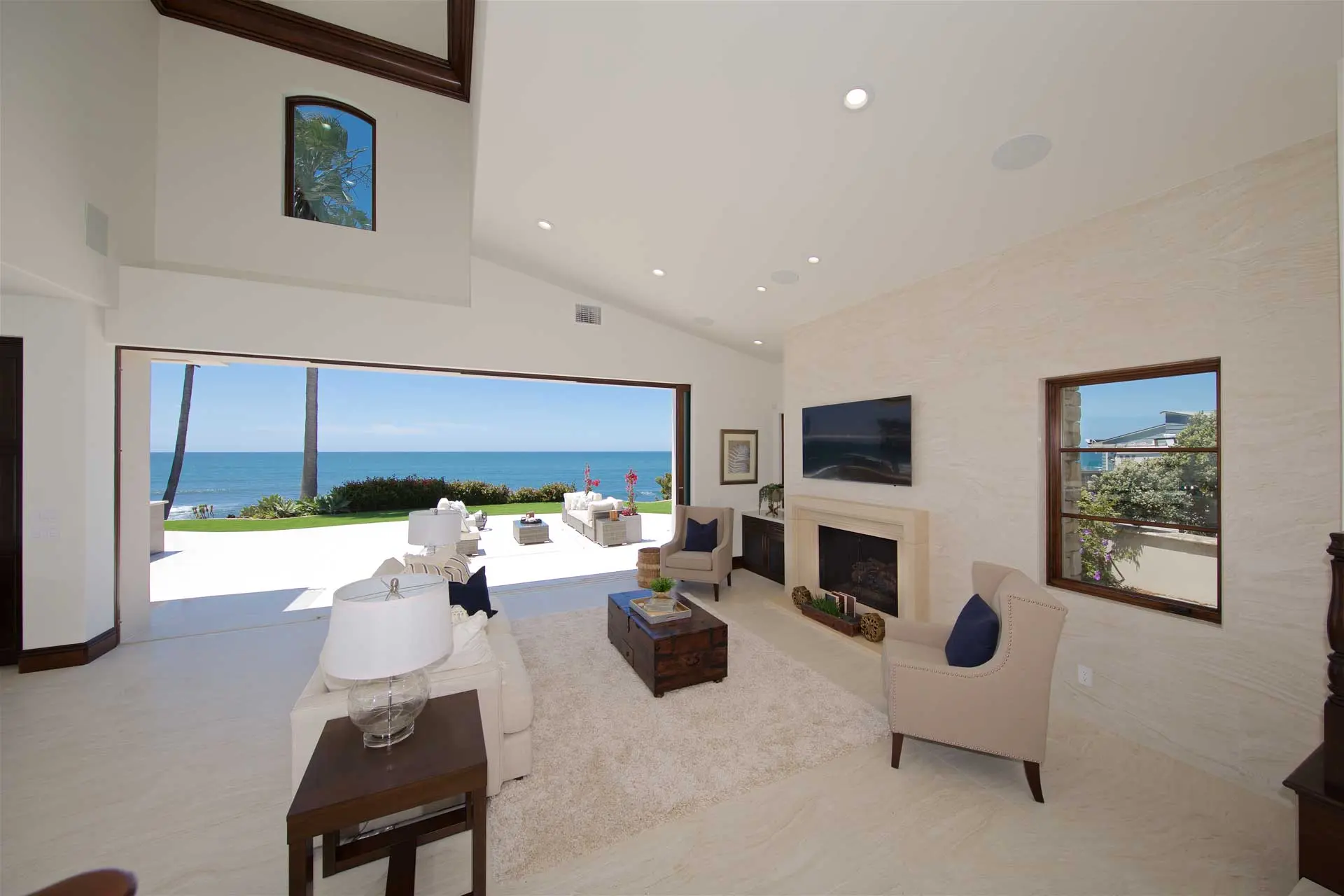 Oceanfront living room with a vaulted ceiling, stone fireplace, and sliding doors framing an ocean view