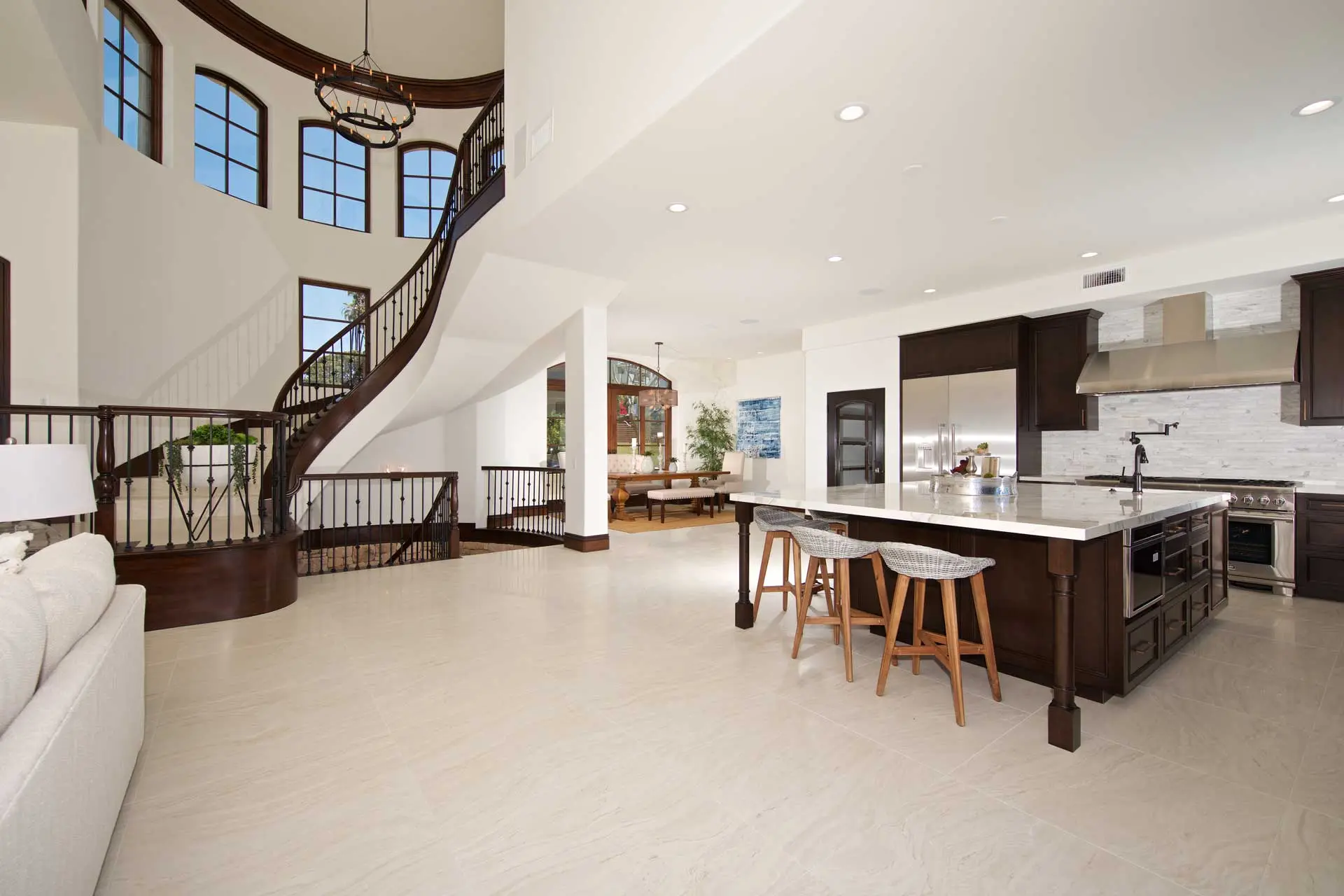 Open-concept kitchen with a large island, dark cabinetry, and a curved staircase in a two-story great room